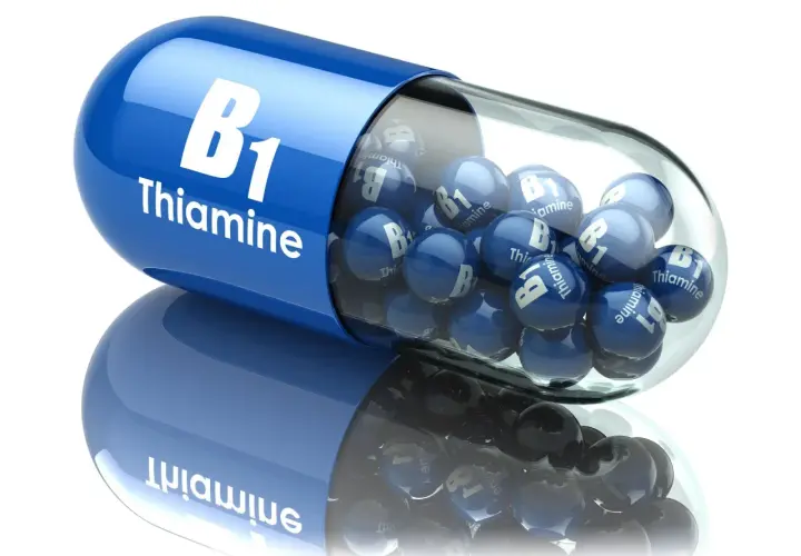 Niebieska kapsułka z napisem "B1 Thiamine" wypełniona małymi kulkami z tym samym oznaczeniem. Tiamina w pigułce.